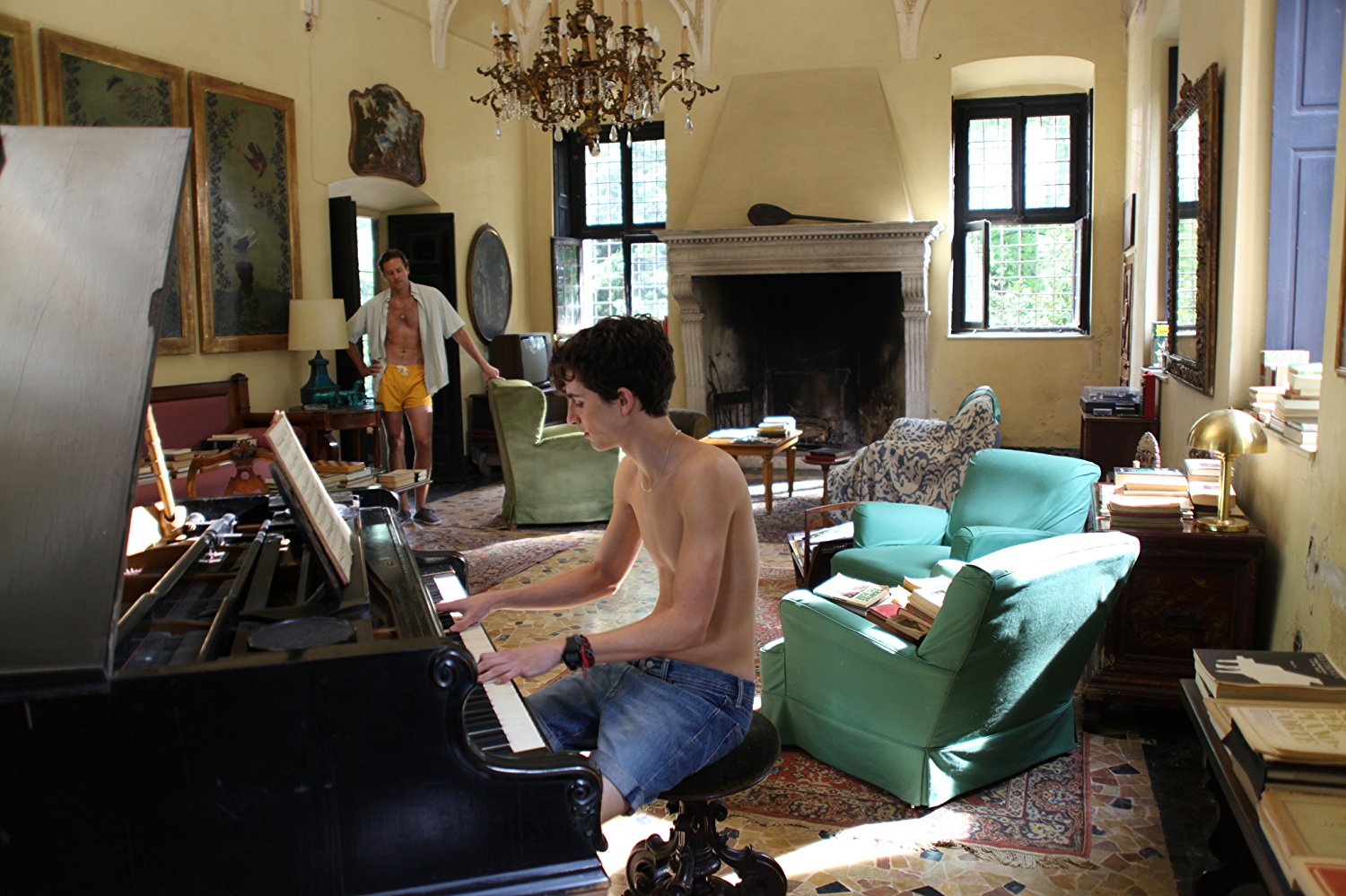 Elio soittaa pianoa, Oliver katselee taustalla. Kuva elokuvasta.